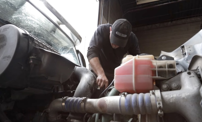 Truck mechanic checking coolant reservoir and engine components